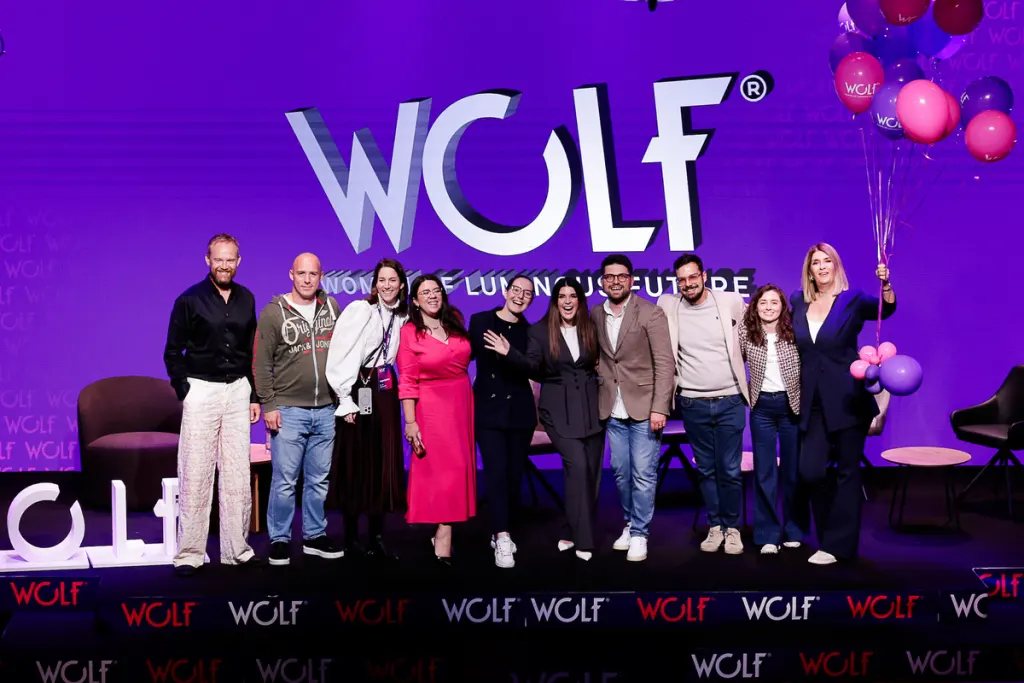 A group of people pose together on a stage in front of a large "WOLF" logo, with balloons and branded decor.